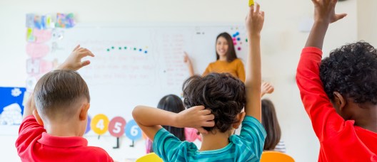 Preschool kid raise arm up to answer teacher question on whiteboard in classroom,Kindergarten education concept